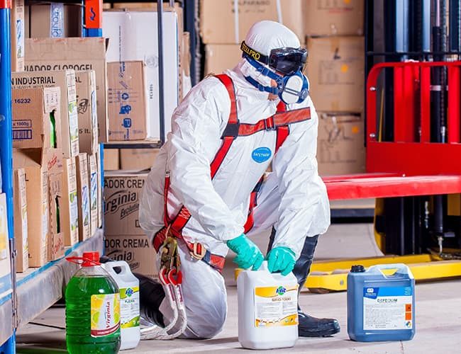 Man in safety suit and bottles of chemicals illustrates PlusChem's expertise in Solvents